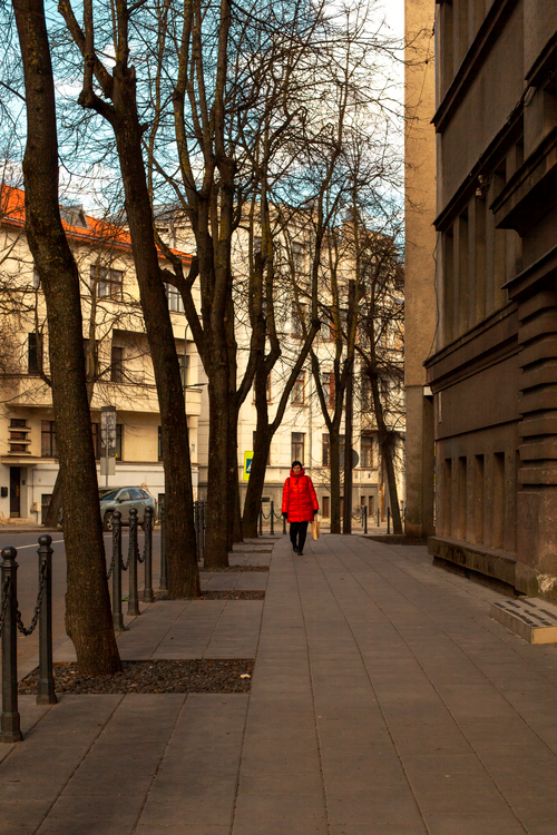 Free City scene with a solitary figure in a red jacket walking through an urban setting in autumn. Stock Photo