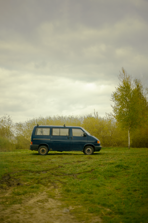 Free A classic van parked in a serene meadow, surrounded by trees under an overcast sky. Stock Photo