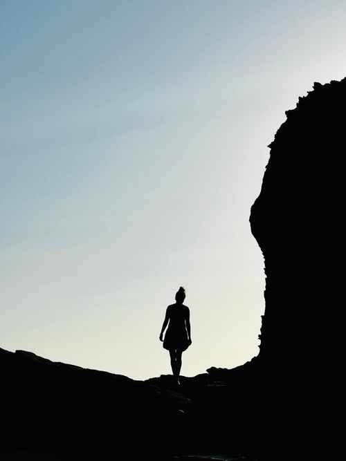 Free A woman silhouetted against a clear sky while hiking near rocky cliffs in Setúbal, Portugal. Stock Photo