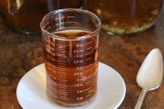 Aromatic herbal tea in a measurement glass on a saucer with jars in background.