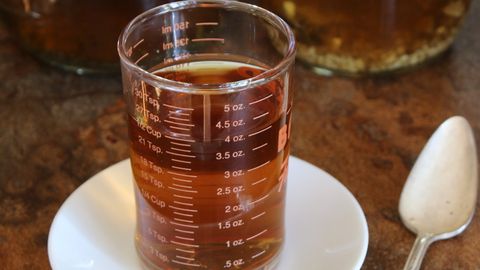 Aromatic herbal tea in a measurement glass on a saucer with jars in background.