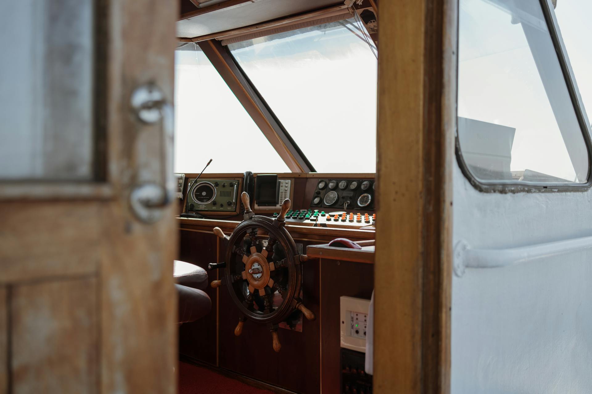 A detailed view of a vintage boat helm featuring a wooden steering wheel and control panels.