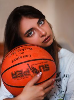 Woman with long hair holding a basketball against her cheek indoors.