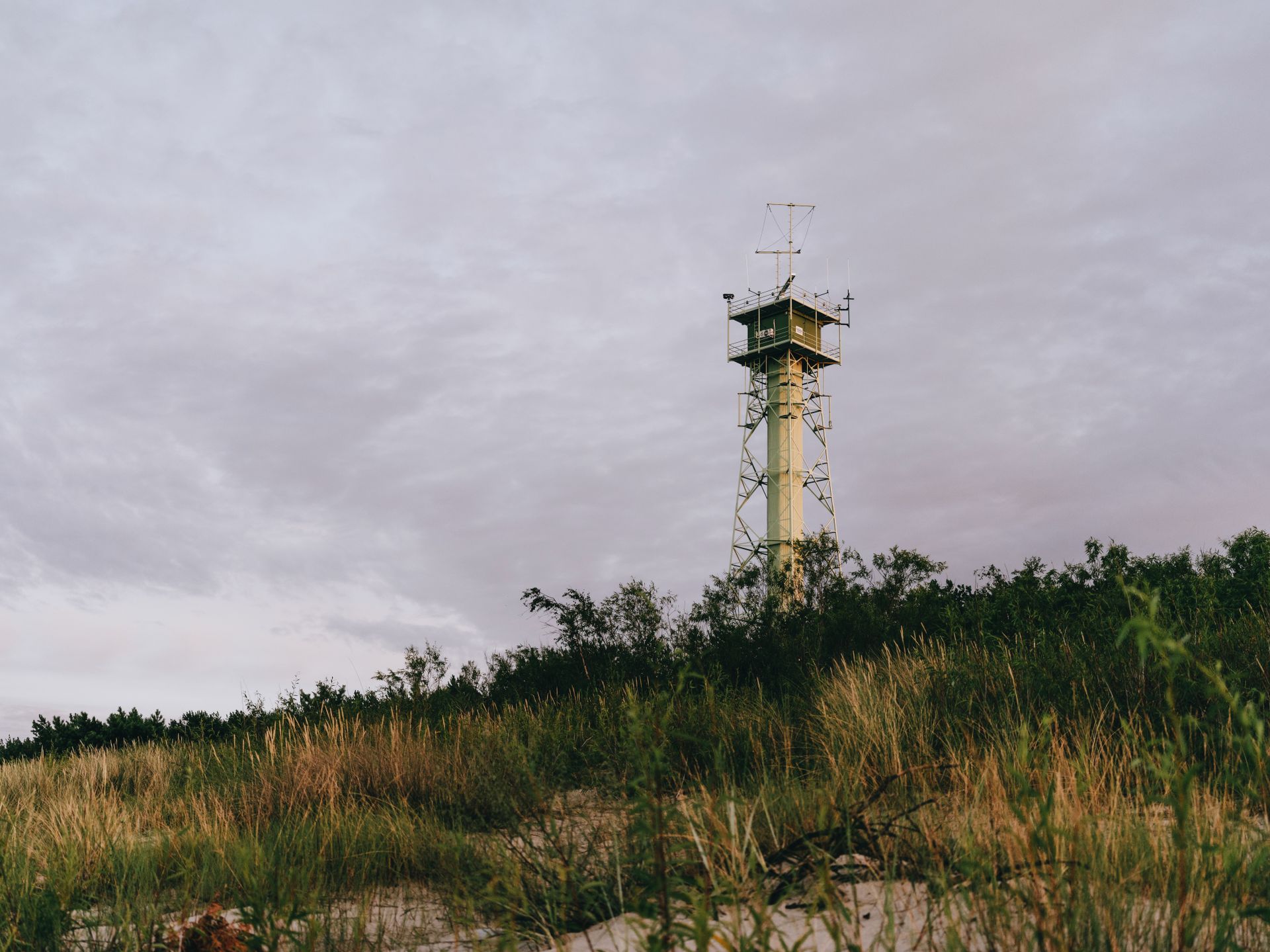 A lone observation tower stands on a grassy hill against an overcast sky, creating a moody scene.