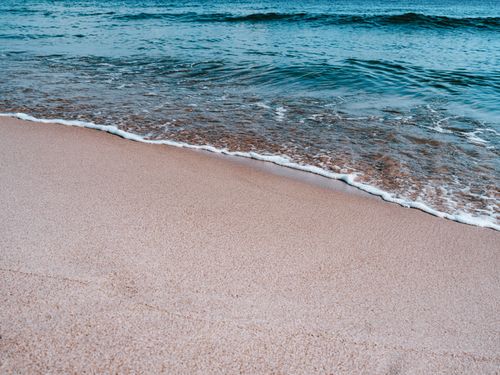 Free A serene sandy beach with gentle waves lapping the shore, perfect for a summer vacation. Stock Photo