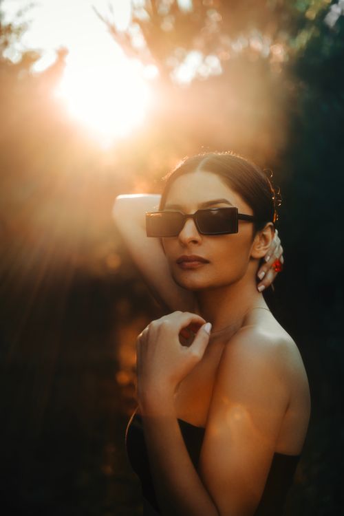 Free A fashionable young woman poses outdoors as the sun sets, wearing stylish sunglasses. Stock Photo
