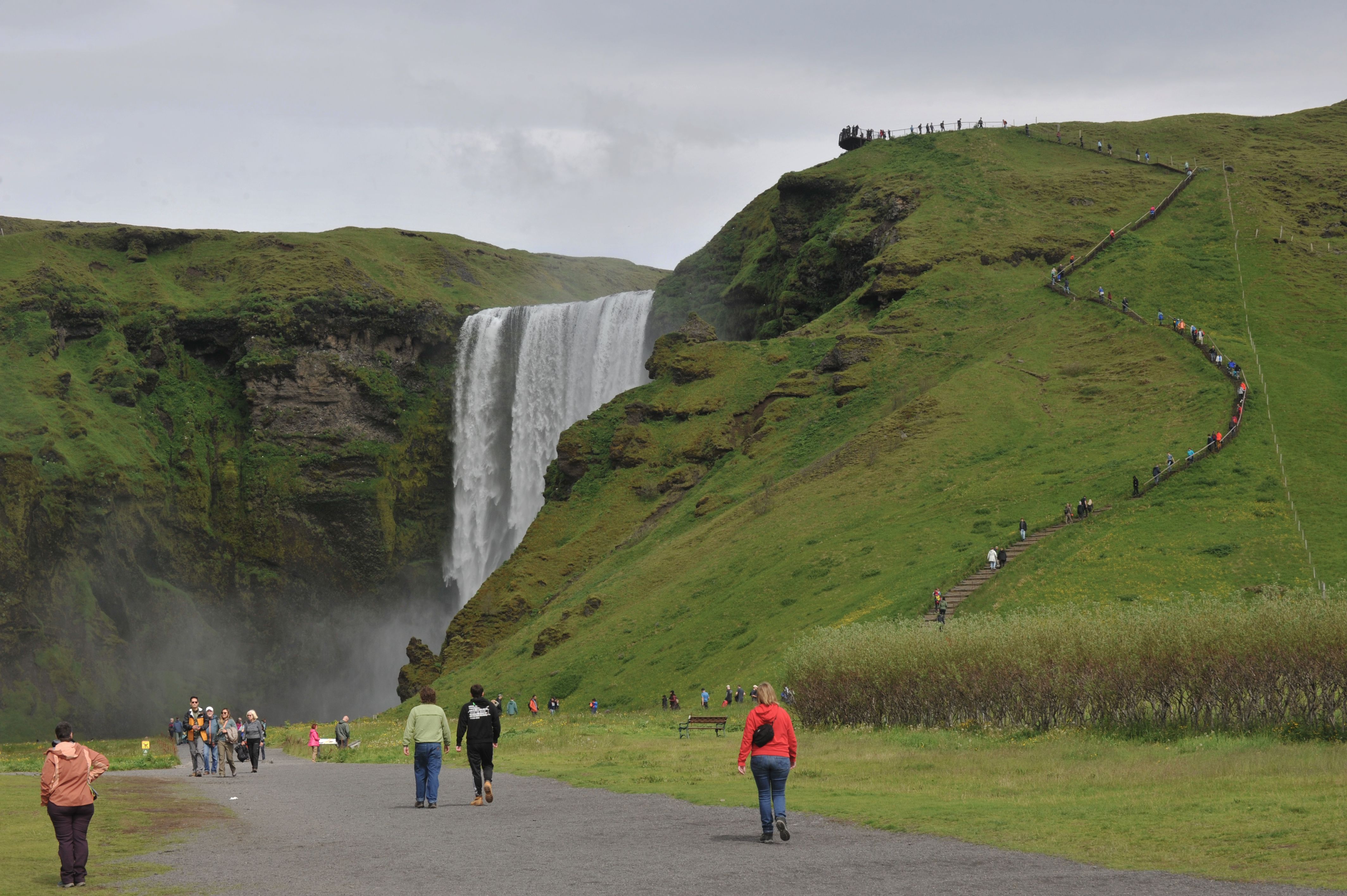 Tourists hiking near an Icelandic waterfall during summer weather