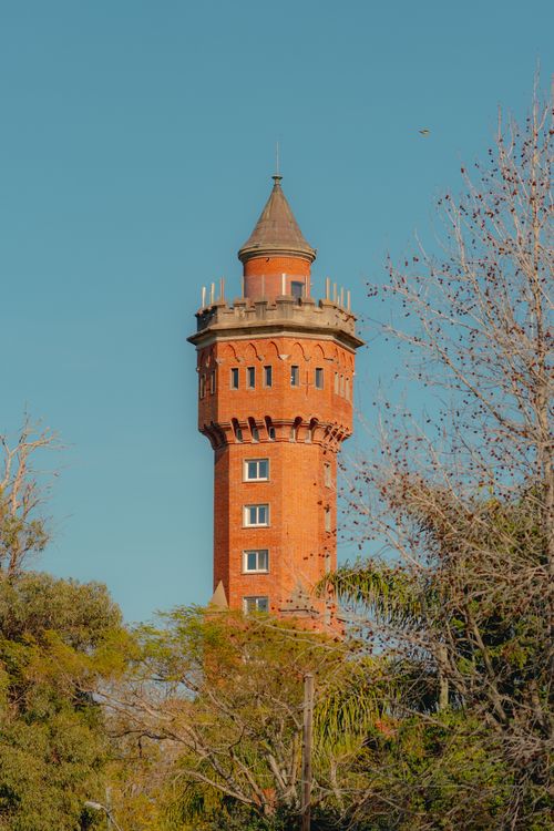 Free Scenic view of a historic brick water tower surrounded by trees under a clear blue sky in Uruguay. Stock Photo