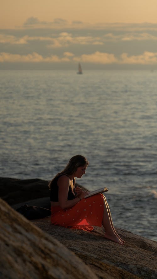 Free Woman Sitting on the Beach and Reading a Book  Stock Photo