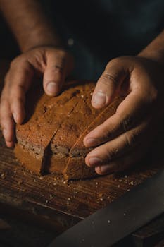 Hands gently holding a loaf of artisan bread on a wooden board in a cozy, rustic setting.