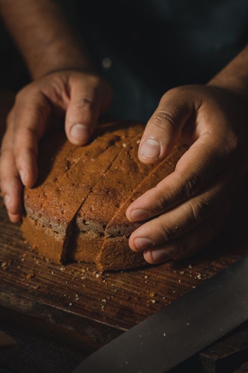 Free Hands gently holding a loaf of artisan bread on a wooden board in a cozy, rustic setting. Stock Photo