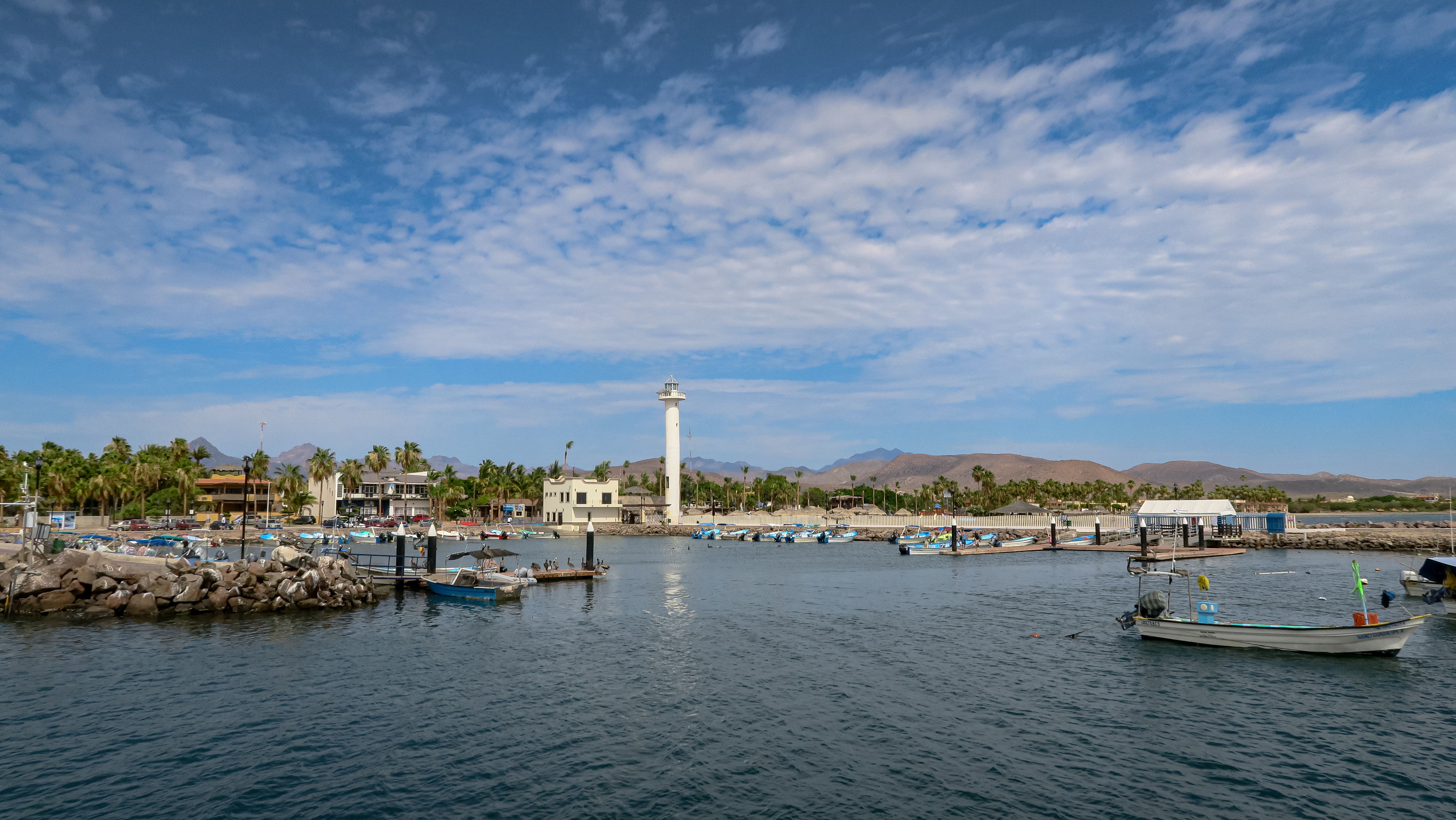 Scenic view of Loreto marina with boats and lighthouse under clear blue skies.