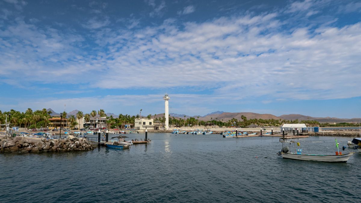 Scenic view of Loreto marina with boats and lighthouse under clear blue skies.