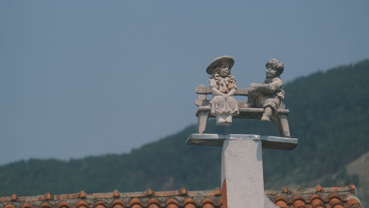 Boy And Girl Figurines On An Old House Roof