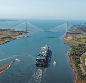 Drone shot of a container ship sailing under a cable-stayed bridge over a river.