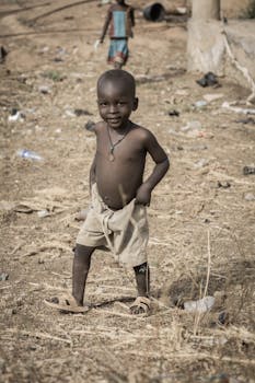 Young boy smiling in a rural area, wearing cotton shorts and sandals.