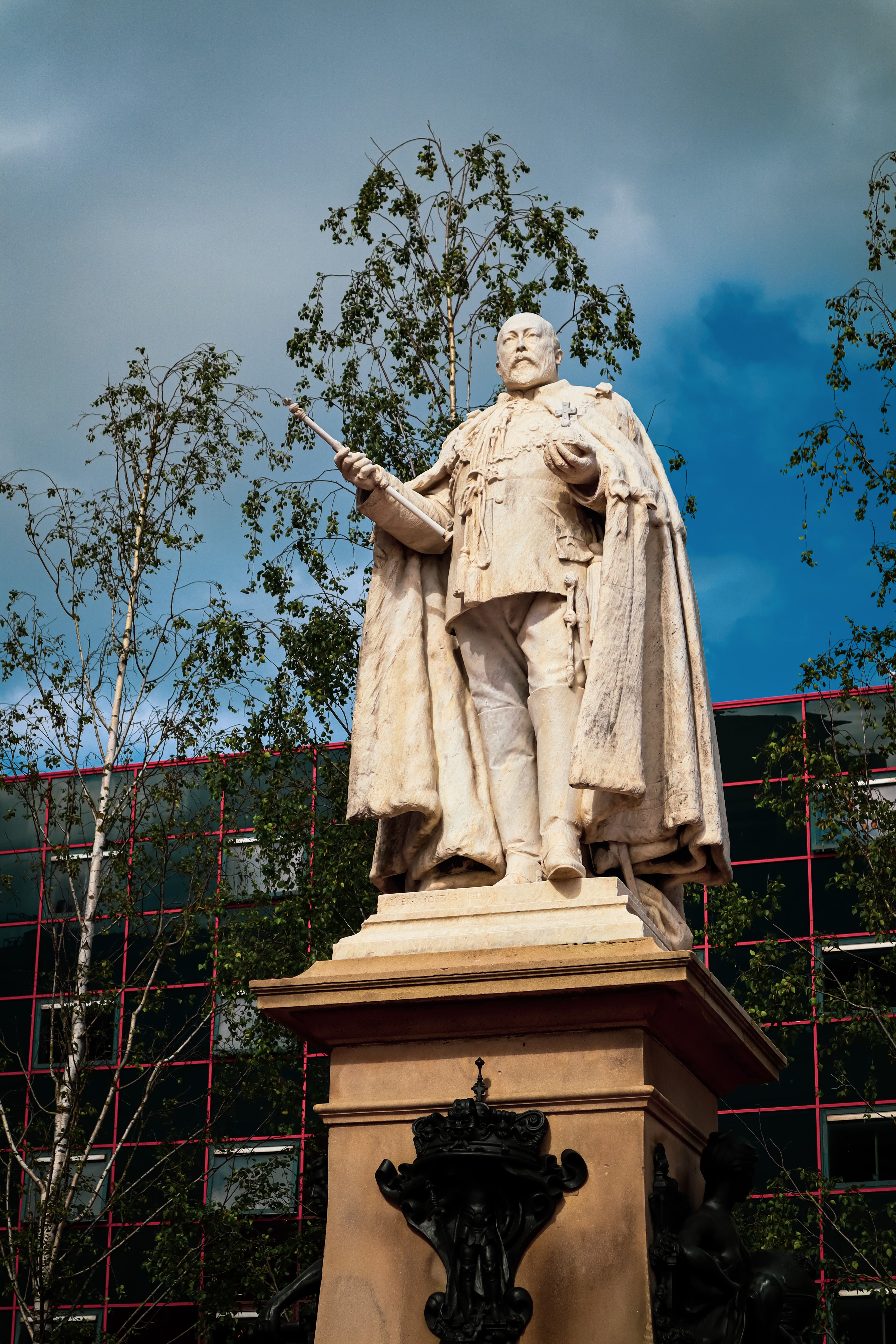 Marble statue of King Edward VII in Birmingham, England, against a backdrop of trees and modern buildings.