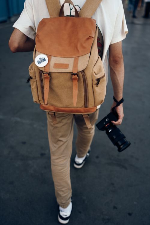 Free Man with a backpack holding a camera walking outdoors, perfect for travel themes. Stock Photo