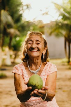 一位戴着珠宝的老妇人，在户外拿着芒果，脸上洋溢着幸福的微笑