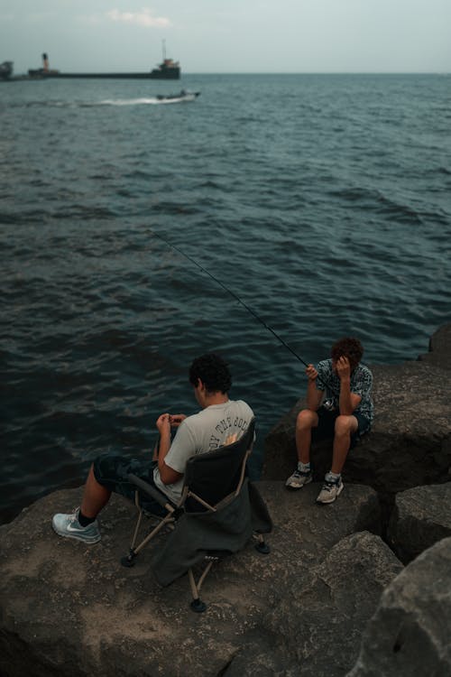Two people sitting on the edge of a cliff looking at the water