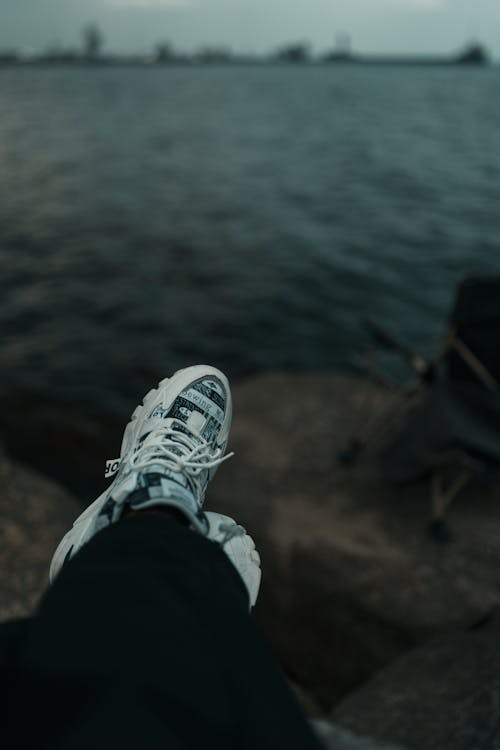 A person's feet are on a rock near the water