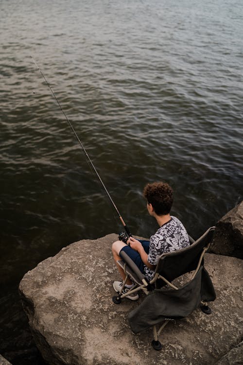 A boy sitting on a rock fishing