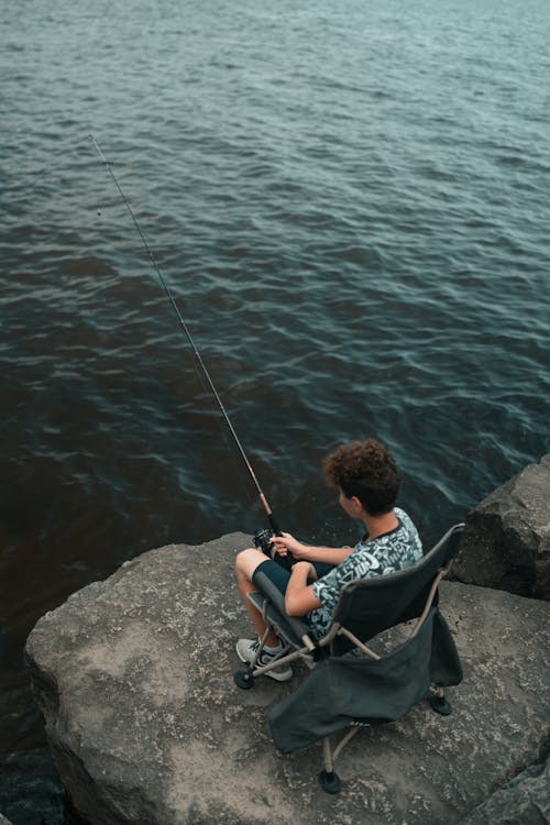 A boy sitting on a rock fishing