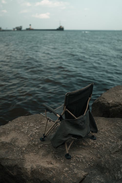 A chair sitting on a rock near the water