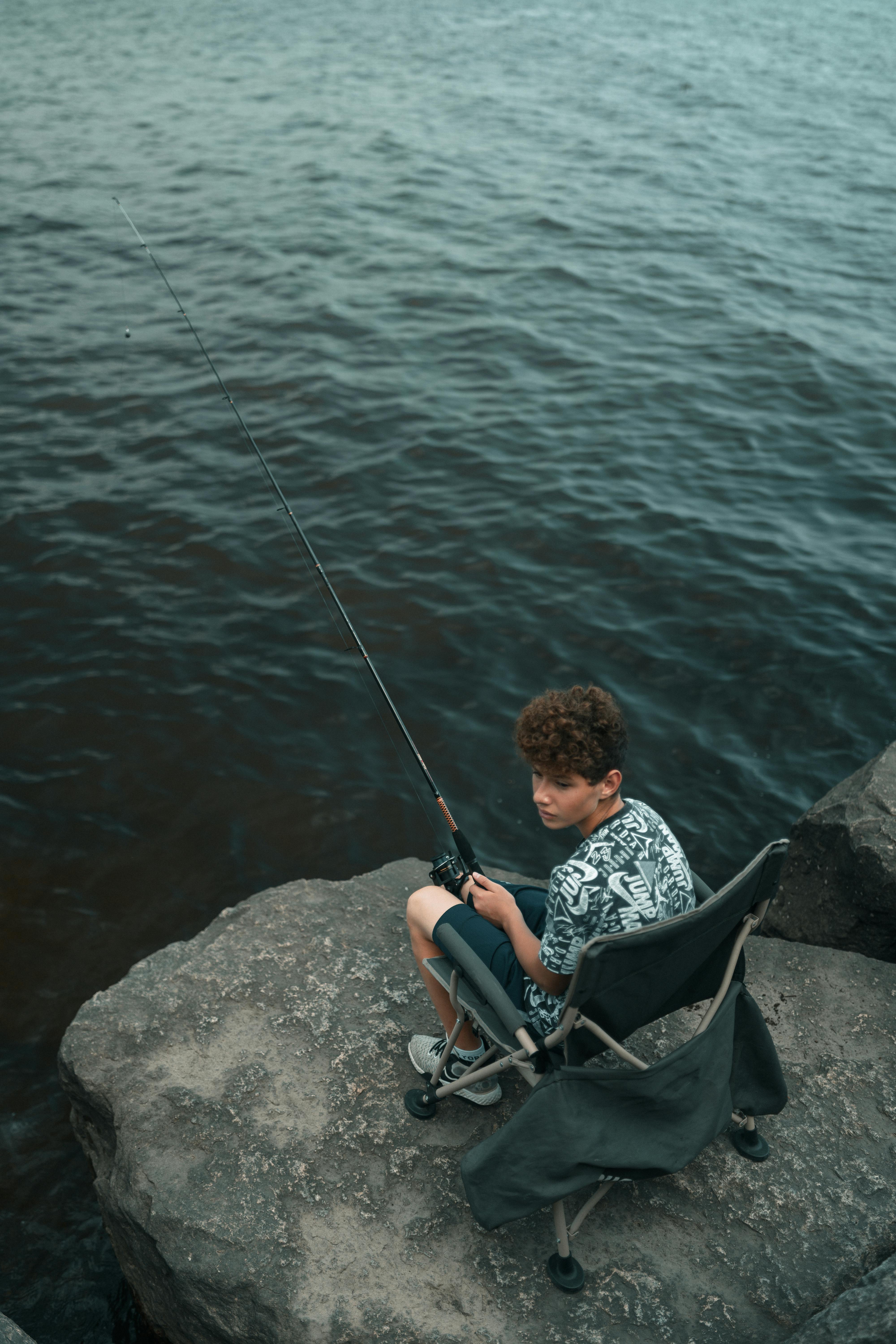 https://images.pexels.com/photos/17863369/pexels-photo-17863369/free-photo-of-a-boy-sitting-on-a-rock-fishing.jpeg