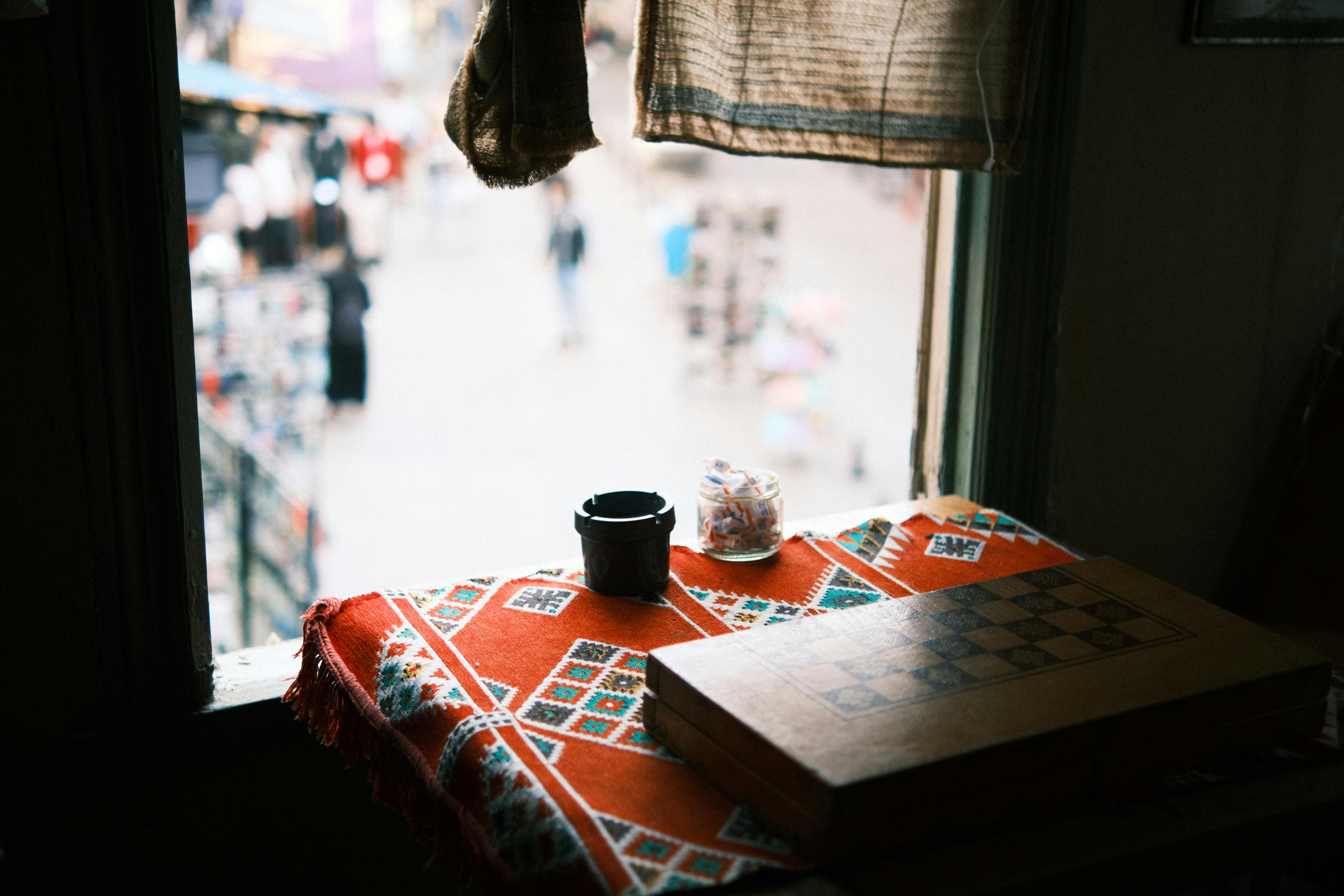 A chess board setup by a window with a colorful tablecloth, creating a warm and inviting atmosphere.