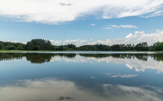 Peaceful lake scene with forest reflection, capturing calm nature and blue sky.