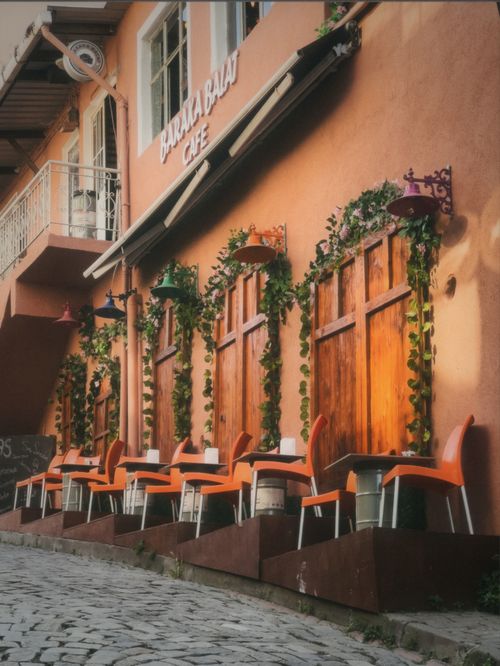 Free Street-side café with vibrant chairs and lush greenery. Stock Photo
