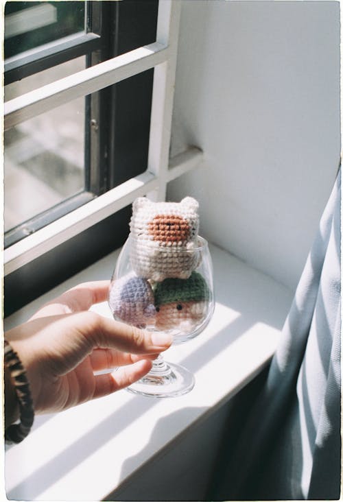 Hand Holding Glass with Toys over Windowsill