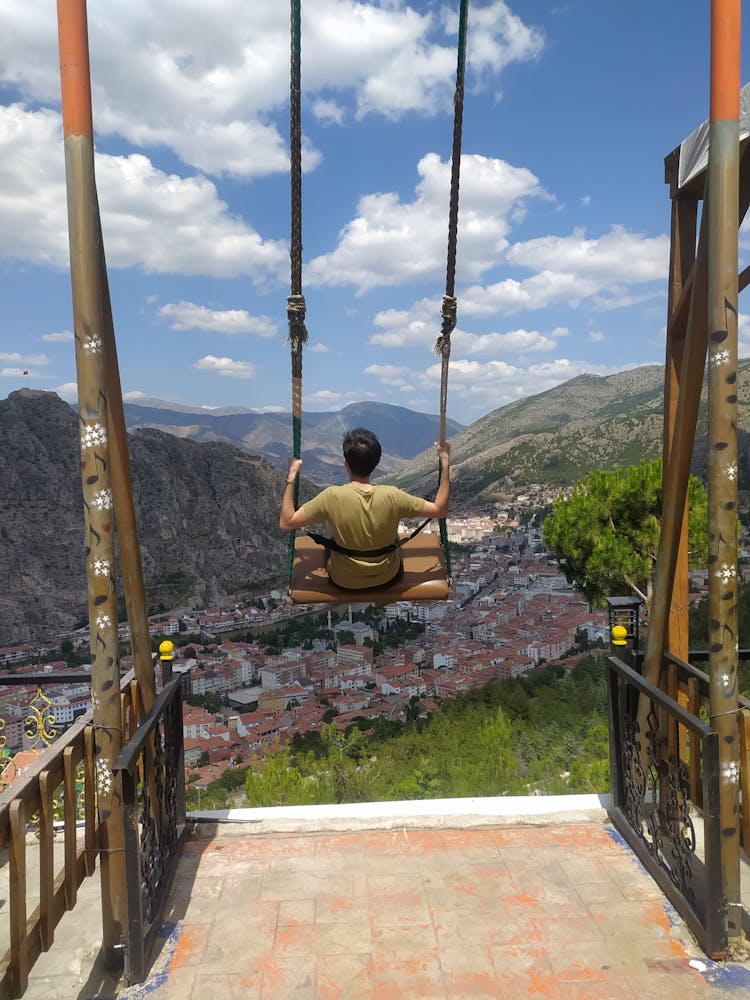 Man Swinging On Swing Over Town In Valley