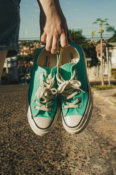 A person holds a pair of green sneakers on a sunny day in Campo Grande, MS, Brazil.