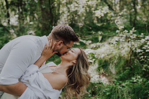 Free Loving couple kissing in a lush green forest, expressing intimacy and joy. Stock Photo