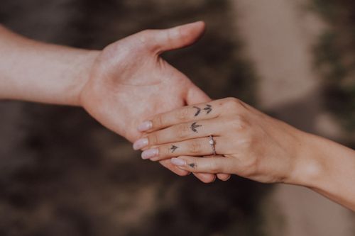 Free Close-up of a couple holding hands showcasing love, tattoos, and an engagement ring. Stock Photo