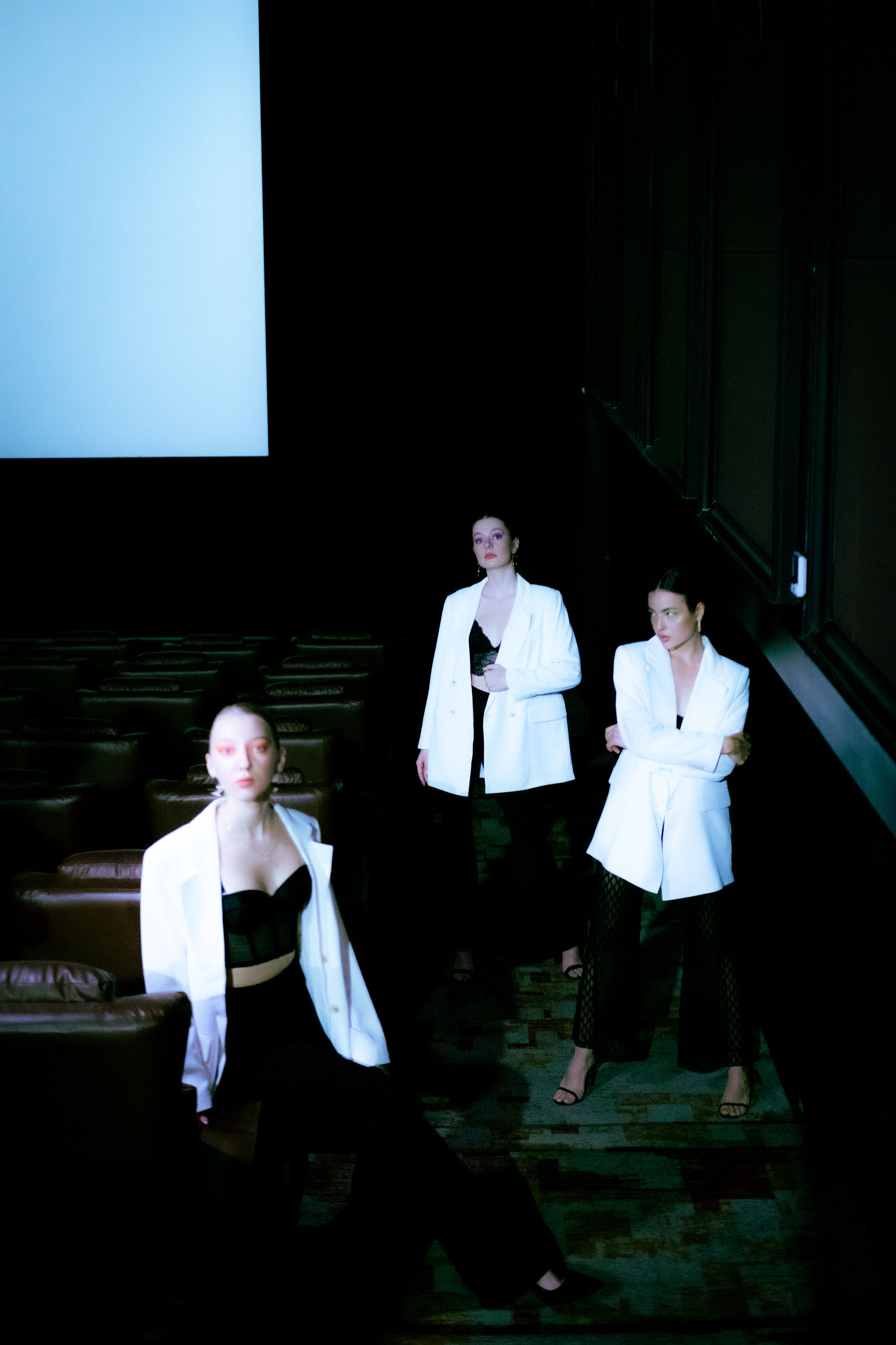 Três modelos posam com roupas estilosas em um teatro, exibindo moda moderna.