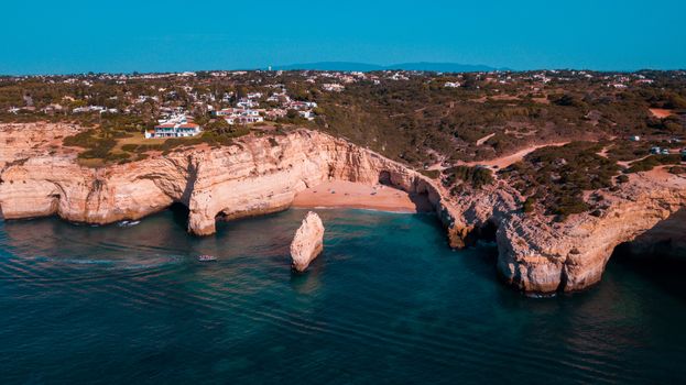 Breathtaking aerial shot of the rugged cliffs along a serene coastline during summer, highlighting clear turquoise waters.