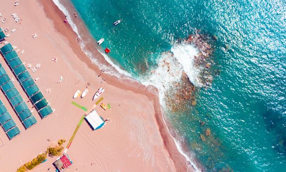 Stunning aerial shot of a beach with boats, colorful waves, and vibrant sand.