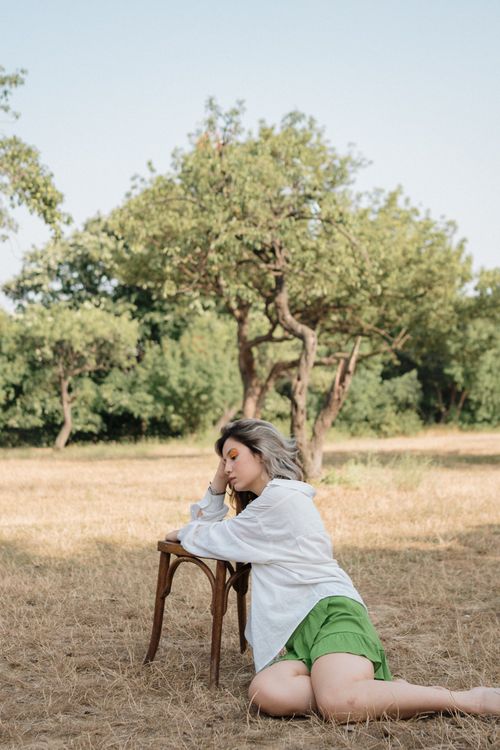 Free A woman kneels beside a chair in a lush orchard, embodying serene tranquility and natural beauty. Stock Photo