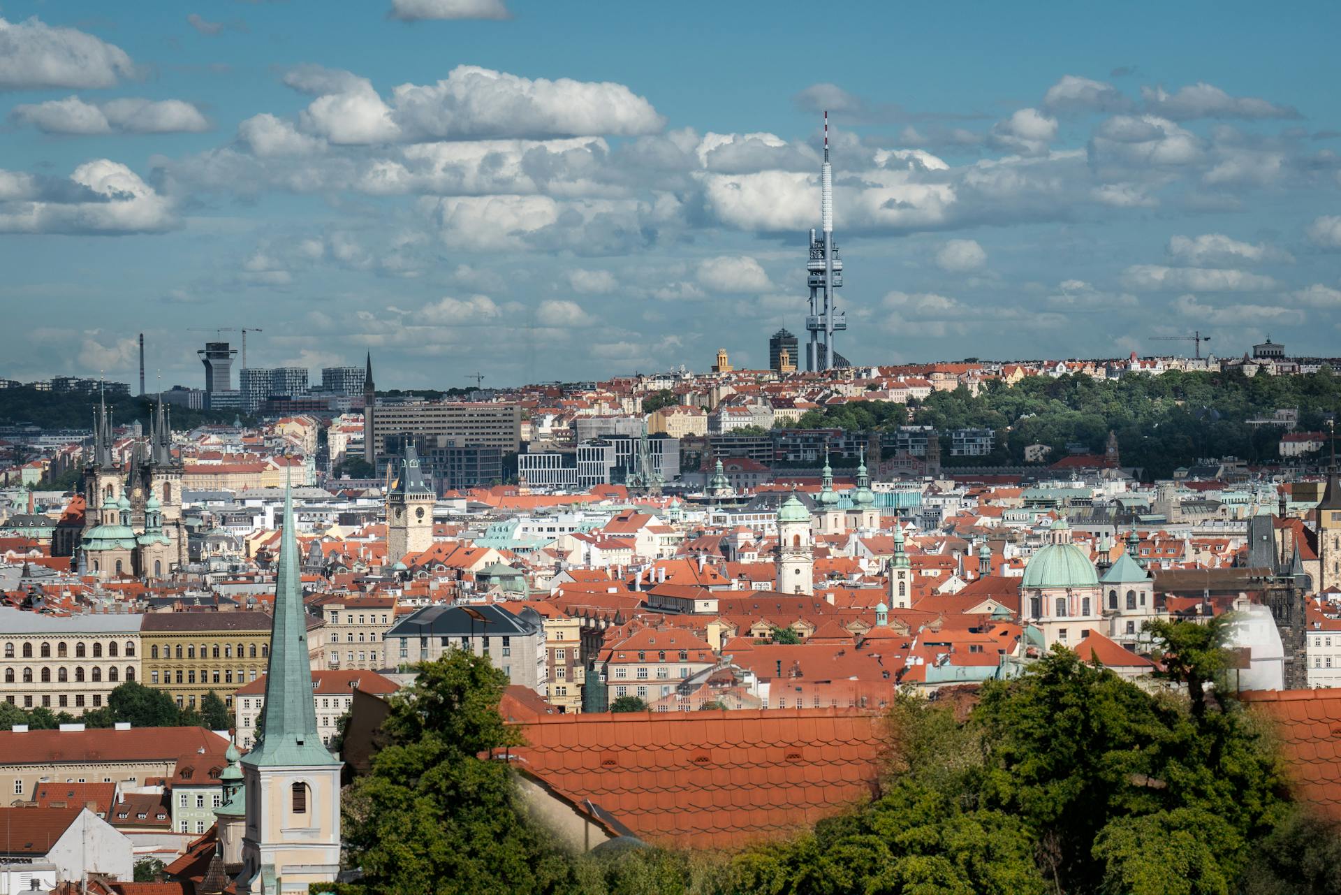 Aerial cityscape of Prague featuring iconic red rooftops and historic architecture on a sunny day.