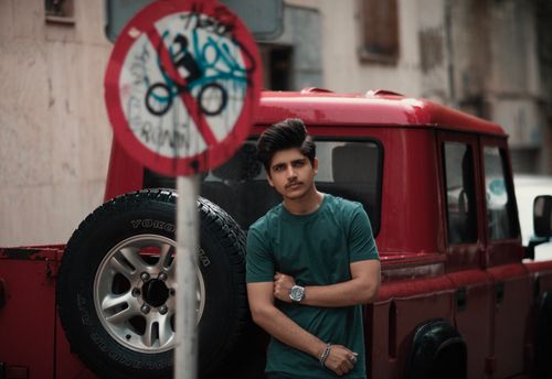 Free Young man posing by a red vehicle in a city street, exuding casual urban style. Stock Photo