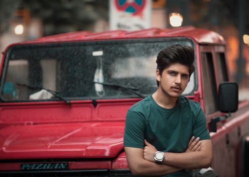 Free Portrait of a young man in front of a red SUV in an urban environment at dusk. Stock Photo