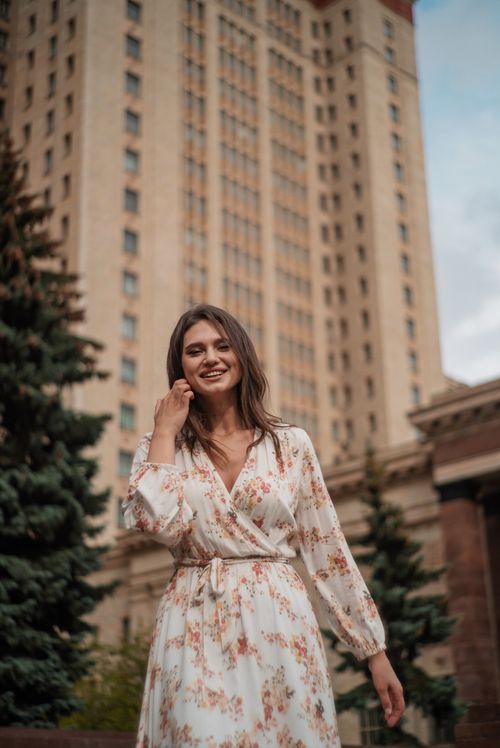 Free Confident woman in a floral dress smiling outdoors against an urban backdrop Stock Photo