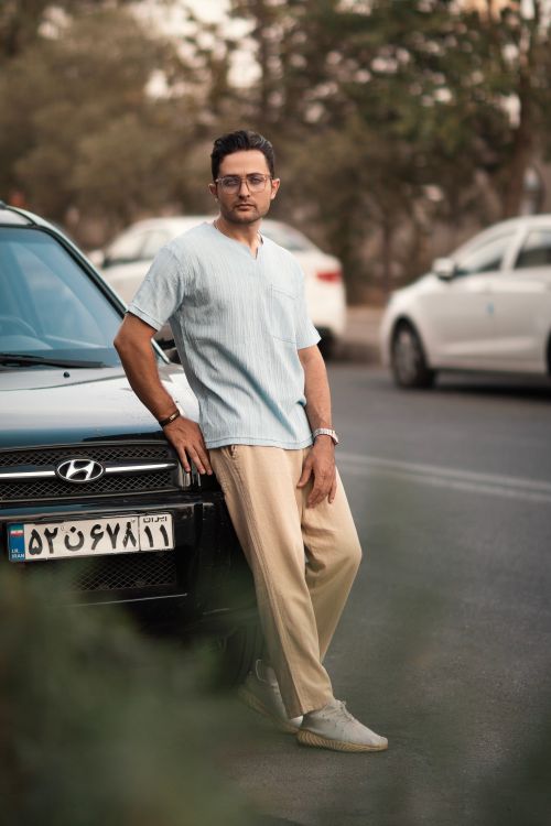 Free Man leaning on a car in a stylish outfit on an urban street, showcasing a casual fashion vibe. Stock Photo