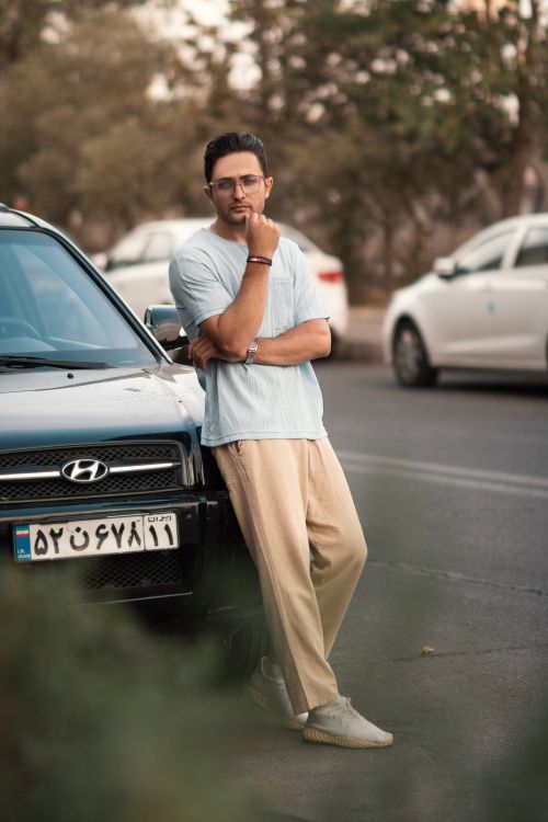 Free A fashionable man poses confidently against a car in an urban street setting, exuding modern style. Stock Photo