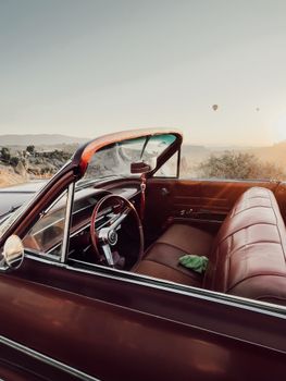 Classic convertible car with hot air balloons at sunrise creating a serene and picturesque view.