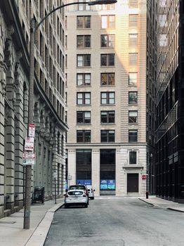 A serene urban street flanked by tall buildings, featuring parked cars and minimal traffic.