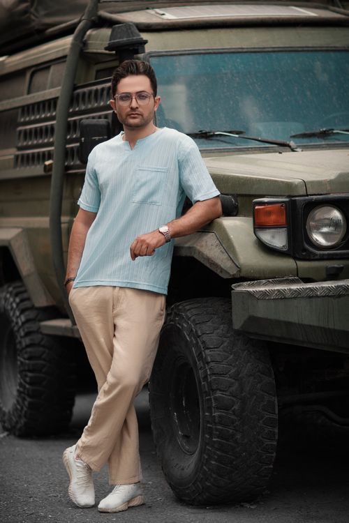 Free A fashionable man in casual attire leans casually against a military vehicle outdoors. Stock Photo